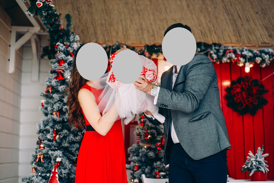 Happy parents and little baby in elegant clothes together in decorated Christmas room.